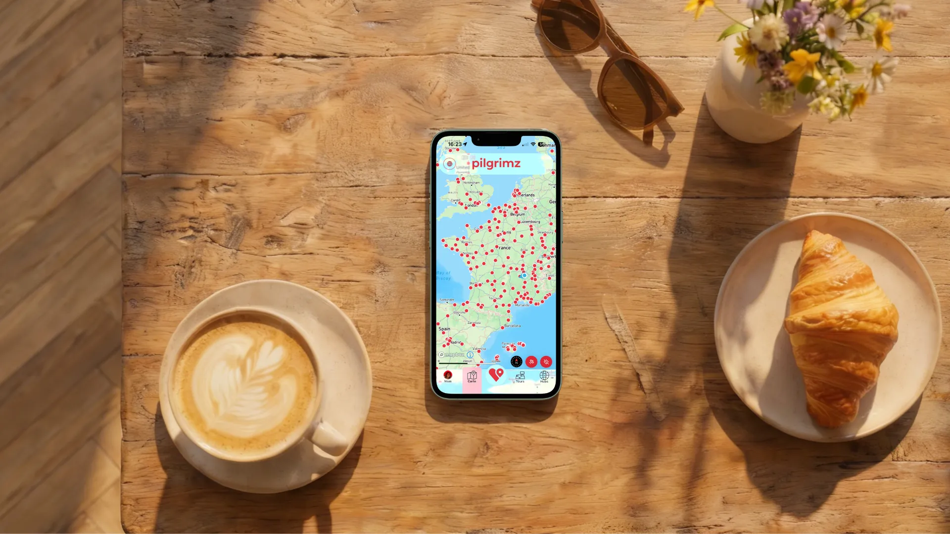 The Pilgrimz app on a phone, with coffee and a croissant